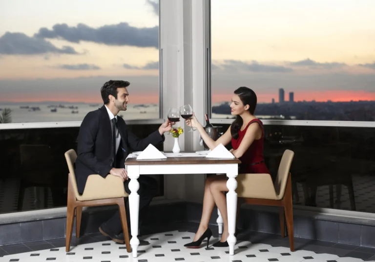 Two guests dining beside a rooftop window at sunset